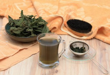 Real nettle tea made from dried nettle,  Urtica diocica, for hair care. Good against dry and damaged hair. Beige wooden table, black brush. 