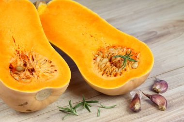 Pumpkin Butternut Liscia cut in half. Yellow delicious pumpkin on wooden table, garlic and rosemary in front. 