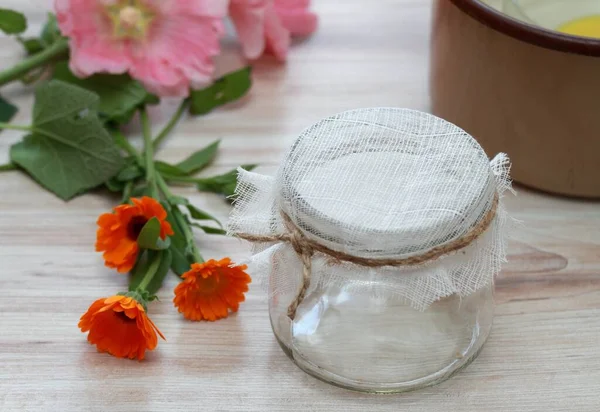 Stuff for home cosmetics. An empty glass ready to filter natural cream good for better skin, Calendula officinalis  in front, Alcea rosea at back.