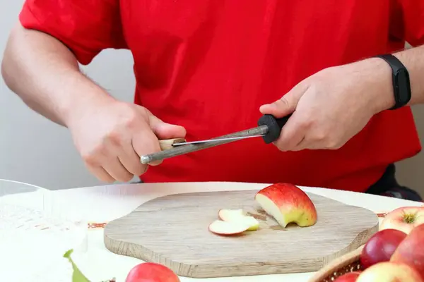 Man sharpening kitchen knife with special tool. Focus on man\'s hands, prepared to cut apples for drying with knife sharpener.