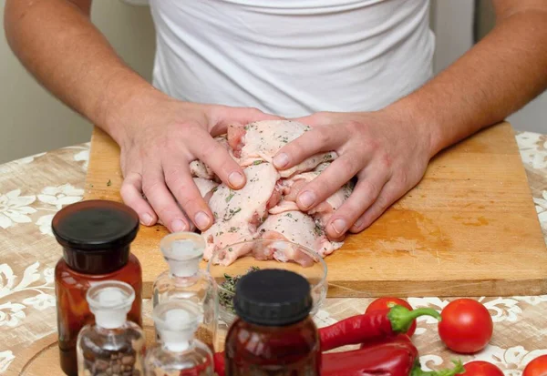 Man's hands and raw chicken meat. Young cook marinates meat with salt, spices and herbs.
