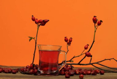 Ahşap masada vitamin dolu gül çayı. Sonbahar havası ve renkler taze gül kalçalarıyla gelir, Kasım yaprakları ve turuncu arka plan.