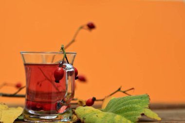 Ahşap masada vitamin dolu gül çayı. Sonbahar havası ve renkler taze gül kalçalarıyla gelir, Kasım yaprakları ve turuncu arka plan.