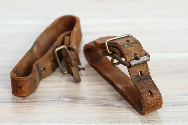 Old leather straps used to tie up skis togetner. Natural leather belts from last century on wooden table.