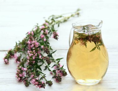 Hissopus 'un taze çiçeklerinden elde edilen bardakta bitki çayı. Hyssopus officinalis. Tahta bir sürahide beyaz bir masada sıcak çay.. 