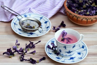 Kurutulmuş yaban ördeği çiçeğinden bir fincan bitki çayı, Lat. Malva sylvestris. Öksürüğe karşı geleneksel şifalı bitki çayı. Kurumuş çiçekler kasenin içinde ve etrafında.