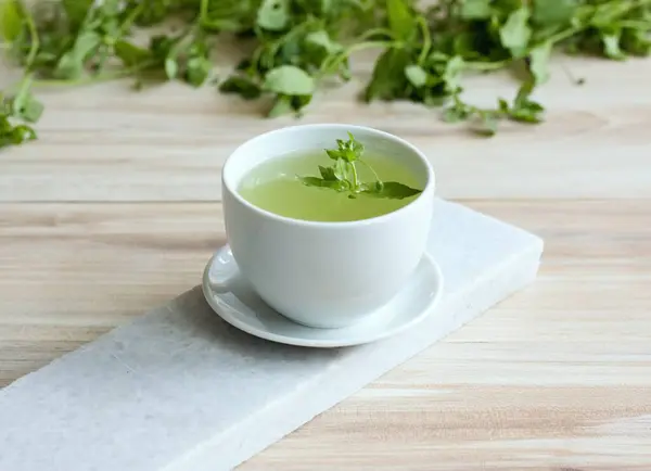 stock image A cup of fresh tea from Chickweed, lat. Stellaria media on white marble. Traditional herb tea rich in minerals is used for detoxificatin, tasty in salads. 