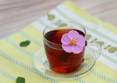 Kaya gülü olarak bilinen Cistus incanus 'tan bir fincan bitkisel karışım. Birçok iç ve dış faydası olan geleneksel bitki çayı. Çayın içinde güzel pembe kayalık gül çiçeği.