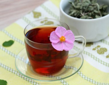 Kaya gülü olarak bilinen Cistus incanus 'tan bir fincan bitkisel karışım. Birçok iç ve dış faydası olan geleneksel bitki çayı. Çayın içinde güzel pembe kayalık gül çiçeği.
