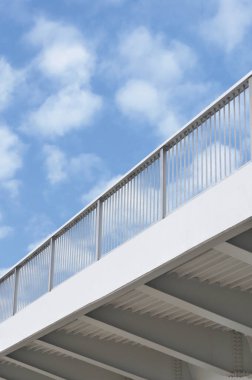 Çelik köprü kiriş açıklığı, mavi gri metal sütun bariyerleri, modern endüstriyel üstgeçit demiryolu perspektifi, geniş detaylı dikey kapatma, boş fotokopi alanı, güneşli yaz gökyüzü bulutları, beyaz bulutlu arka plan görünümü