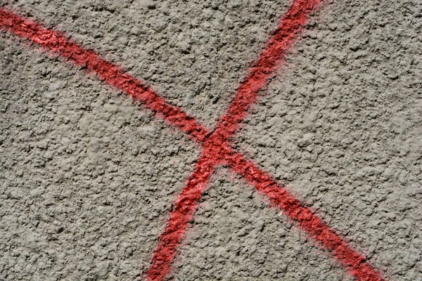 Detail of a gray building exterior wall with red paint cross