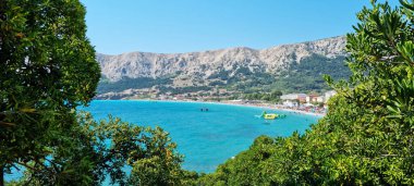 Hırvatistan 'ın Krk adasındaki Baska' daki ana plaj (Vela Plaza) ağaçlarının arasından bak