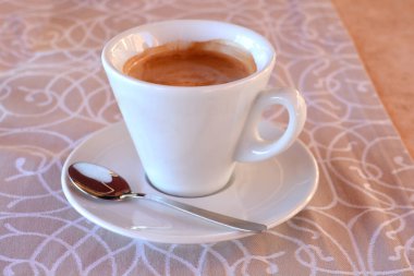 Beyaz bir kahve fincanı ve kaşık desenli masa örtüsü olan bir fincan tabağı.