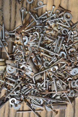 Çeşitli vidalar, fındıklar, farklı boyutlarda ve şekillerde yıkama makineleri, bazıları paslı, ahşap bir masa üzerinde karıştırılmış.