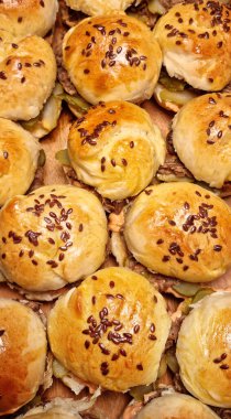 Yırtık domuz etiyle dolu üst aşağı manzara, yan yana dizilmiş, keten tohumları serpiştirilmiş çörekler.