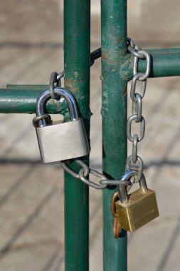İki asma kilit, bir gümüş ve bir altın, yeşil metal bir çitin etrafına zincirlenmiş.