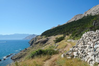 A hiking trail winds along the western edge of Baska Bay in Croatia, offering picturesque views of the Adriatic Sea and the surrounding rocky landscape clipart