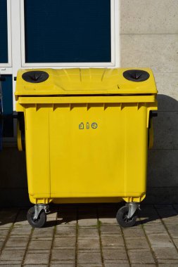 Bir binanın önündeki asfalt bir yüzeye yazılan sarı plastik geri dönüşüm kabı.