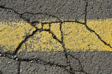 Yol hasarı, aşınma ve yırtılmayı gösteren sarı çizgili çatlak bir asfalt.