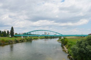 A scenic view of the Green Railway Bridge, also known as Hendrix Bridge, spans the Sava River in Zagreb, Croatia, under a partly cloudy sky clipart