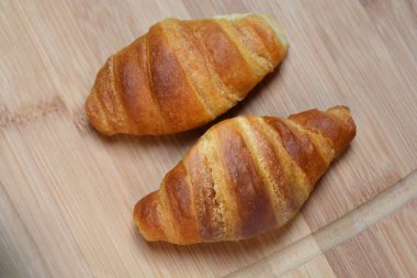 Tahta kesme tahtasının üzerinde iki altın rengi kruvasan sergileniyor.