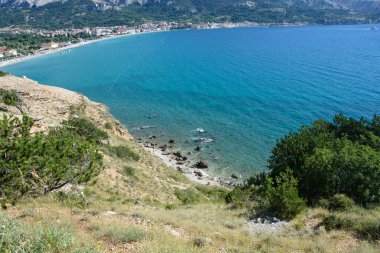 Baska sahili (Vela plaza) ve Hırvatistan 'ın Baska Körfezi' nin kayalık batı kıyısından görüldüğü gibi mavi deniz kıyısında yer alan aynı isimli köy manzarası