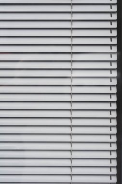 Paralel çizgilerini ve ince gölgelerini gözler önüne seren kapalı beyaz metal yatay perdeler.