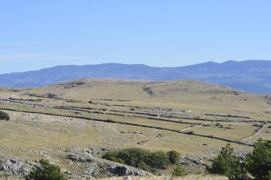 Hırvatistan 'ın Krk adasında Baska' dan Vela Luka 'ya uzanan manzaralı bir yürüyüş yolu, uzak mesafede geleneksel kuru taş duvarları olan engebeli, kayalık bir arazide esiyor.