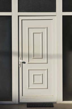 Binanın ön cephesinde koyu renkli cam paneller olan beyaz panelli bir kapının ön çekimi.