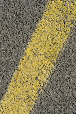 Kaba, gri asfalt yüzeyinde sarı bir çizginin yakın çekimi.