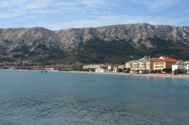 Hırvatistan 'ın Baska kentindeki Vela Plaza (Büyük Plaj) adlı sakin bir sonbahar sahnesinde, kıyı köyü ve kayalık dağlara karşı sakin bir deniz manzarası yer alıyor.