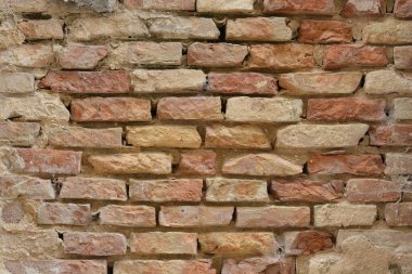 Eski bir tuğla duvarın desenli, yakın çekim görüntüsü. Duvarın yıpranmış ve eskimiş görünümünü gösteriyor. Kırmızı ve bej tonlarında.