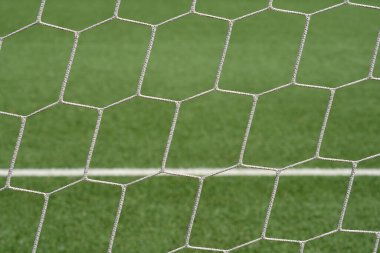 Arka planda yeşil bir alan ile yakın plan bir futbol gol ağı görüntüsü, ağın dokusu ve desenlerine odaklanarak,