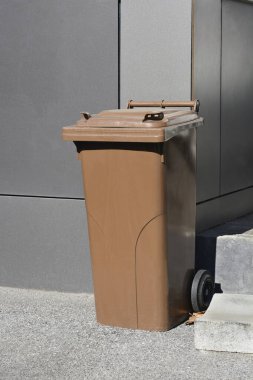 Organik atık toplama için kahverengi bir gübre kutusu dışarıda nötr bir arka planda duruyor.