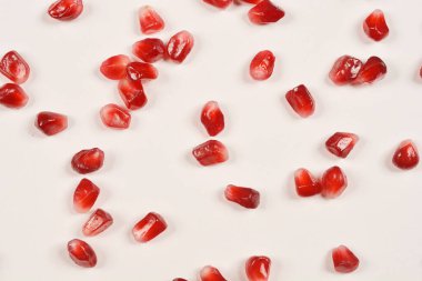 Dağınık kırmızı nar çekirdekleri beyaz bir zemin üzerinde parlıyor.