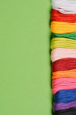 Yeşil arkaplanın sağ kenarı boyunca düzenlenmiş renkli nakış ipliklerinin dikey çekimi, sol tarafta geniş bir boşluk var.