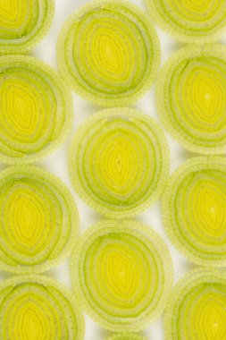 Dilimlenmiş pırasa mermilerinin yukarıdan aşağıya yakın görüntüsü, eşmerkezli dairelerini ve şeffaf dokusunu gösteriyor.