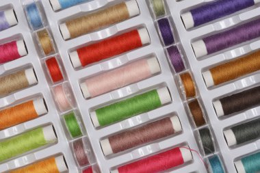 Beyaz plastik bir kutuya yerleştirilmiş renkli dikiş ipliklerinin yakın plan çekimi.