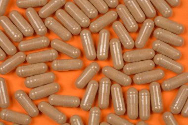 Parlak turuncu bir yüzeye saçılmış sayısız bej kapsülün yukarıdan aşağı görüntüsü, dokularını ve miktarlarını vurguluyor.