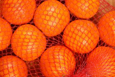 Kırmızı bir çantadaki birkaç portakalın yakın plan fotoğrafı, canlı renklerini ve dokulu derilerini gösteriyor.