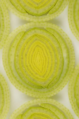 Dilimlenmiş pırasa mermilerinin yukarıdan aşağıya yakın görüntüsü, eşmerkezli dairelerini ve şeffaf dokusunu gösteriyor.