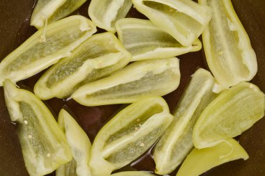 Dilimlenmiş açık yeşil dolmalık biberlerin yukarıdan aşağı görüntüsü. Koyu bir tavaya dizilmiş.