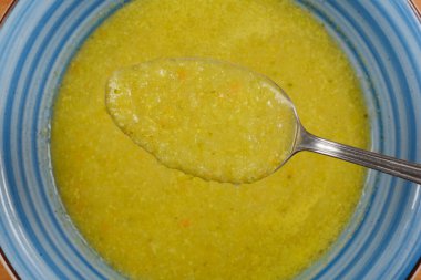 Bir kaşık kremalı brokoli çorbası mavi çizgili bir tabaktan kaldırılır ve pürüzsüz dokusunu ve canlı yeşil rengini gösterir.