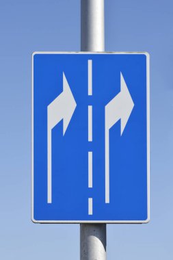 Sağ tarafta beyaz oklar ve mavi arka planda metal bir direğe monte edilmiş kesik bir çizgi olan bir trafik işaretinin yakın çekimi.