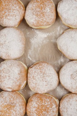 Üzerinde toz şeker serpiştirilmiş taze pişmiş çöreklerin detaylı bir genel çekimi, hafif bir yüzey üzerinde sıralanmış, bir donut eksik