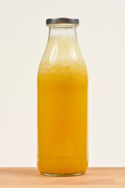 Sarı meyve suyuyla dolu, metal bir kapakla dolu bir cam şişenin stüdyo çekimi tarafsız bir arkaplana karşı ahşap bir yüzeye yerleştirildi.