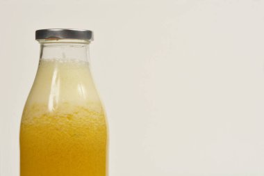 Taze portakal suyuyla dolu bir cam şişenin yakın çekimi, metal bir kapakla, tarafsız bir arkaplan üzerine kurulmuş.