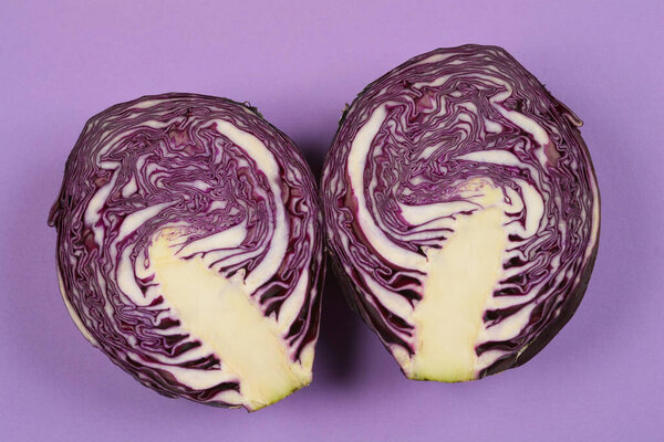 A close-up shot of a red cabbage cut in half, revealing its vibrant purple and white layers against a solid purple background