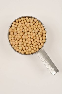 Paslanmaz çelik ölçü kabının yukarıdan aşağı görüntüsü açık arkaplanda kuru soya fasulyesiyle dolu.
