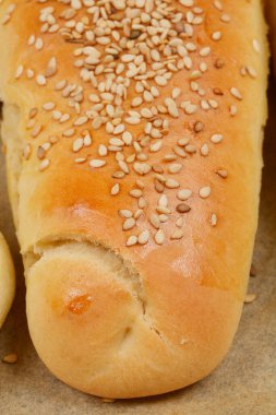 Üzerinde susam tohumları serpiştirilmiş, altın-kahverengi kabuğunu gösteren yakın çekim hamur rulosu.
